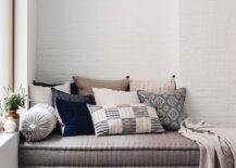 Window seat bench with gray cushions is next to tree trunk accent tables on a black fringe rug.