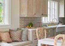 Welcoming kitchen features a brushed oak built-in window seat donning drawers with brass pulls and topped with a tan seat cushion complemented with an assortment of pillows.