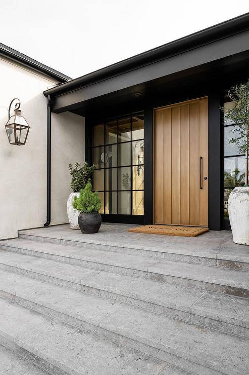 A welcome mat sits in front of a beige plant front door flanked by windows.