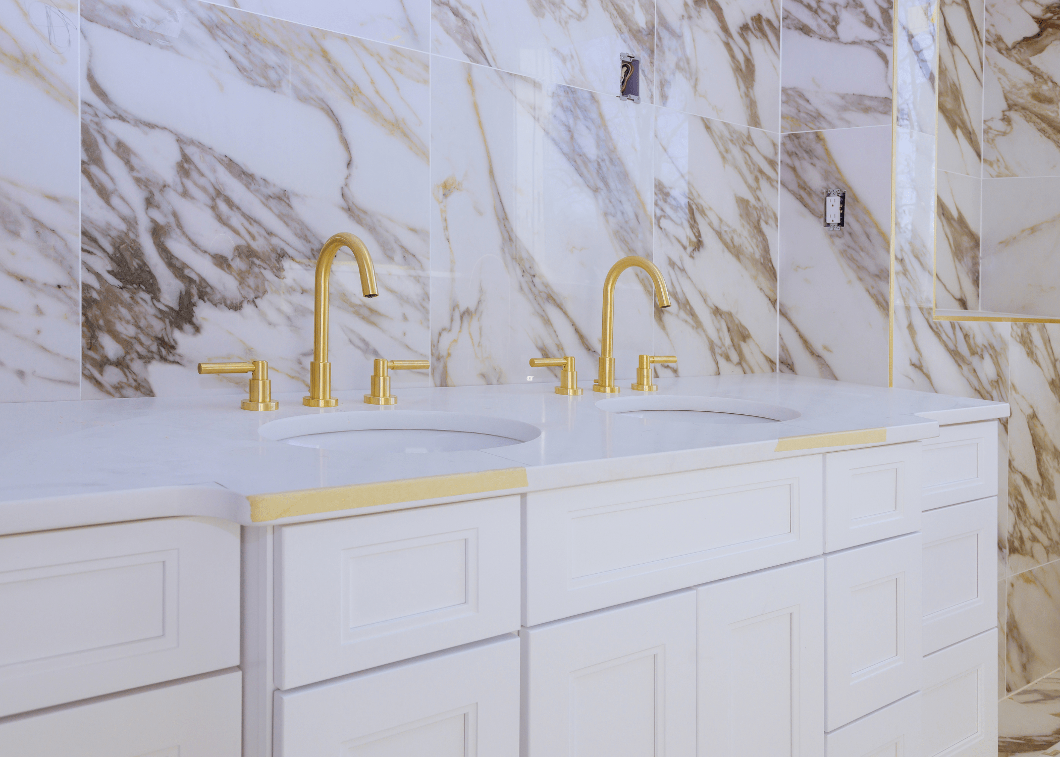 white bathroom countertop with gold faucets and marble backsplash