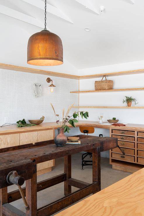 Cottage work space features a vintage work table, wooden shelves, white peg boards and vintage wooden drawers.