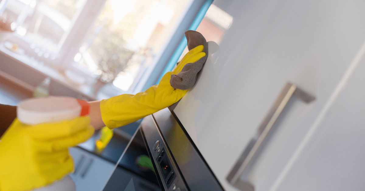 Person wearing yellow gloves cleaning kitchen cabinets.