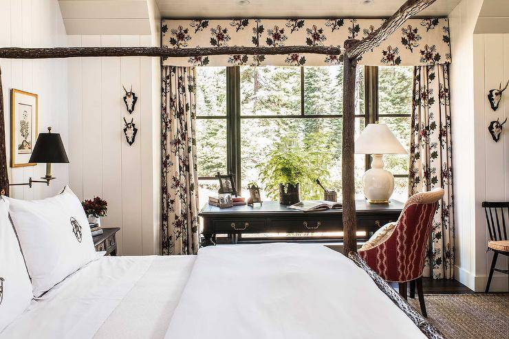 Elegant bedroom work space features a red desk chair placed at a black French desk topped with a white gourd lamp and positioned in front of windows dressed in floral curtains with a matching valance.