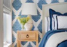 Thibaut Palampore Leaf wallpaper accents a restful white and blue bedroom featuring an off-white curved headboard supporting a bed covered in white and blue bedding topped with white and blue pillows.