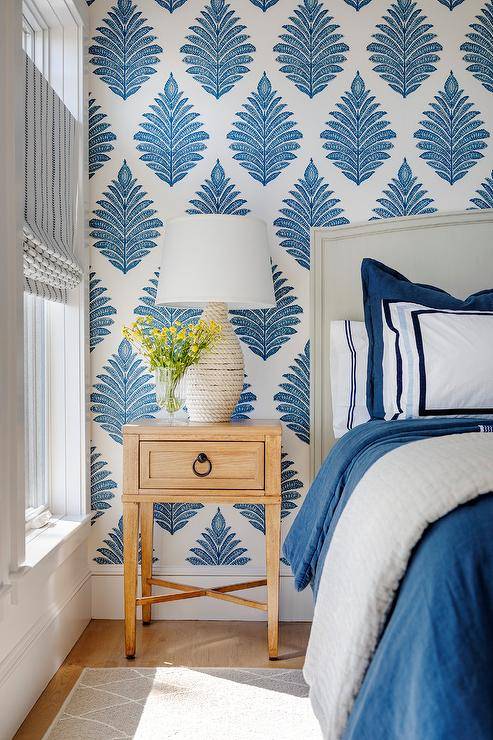 Thibaut Palampore Leaf wallpaper accents a restful white and blue bedroom featuring an off-white curved headboard supporting a bed covered in white and blue bedding topped with white and blue pillows.