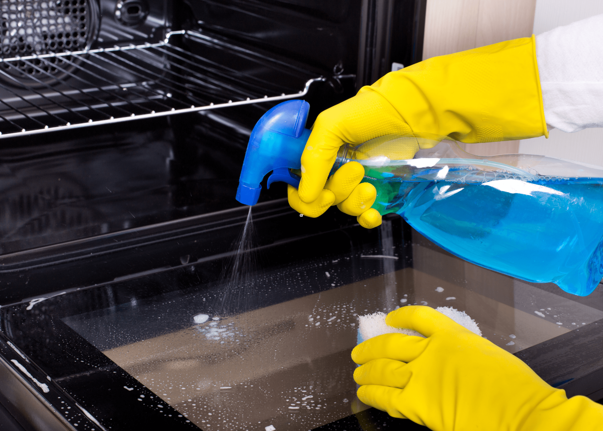 spraying an oven with a blue spray bottle