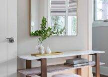 Entryway features a pink marble shelf console table under a mounted brass arch mirror with a white and brown wooden stool.