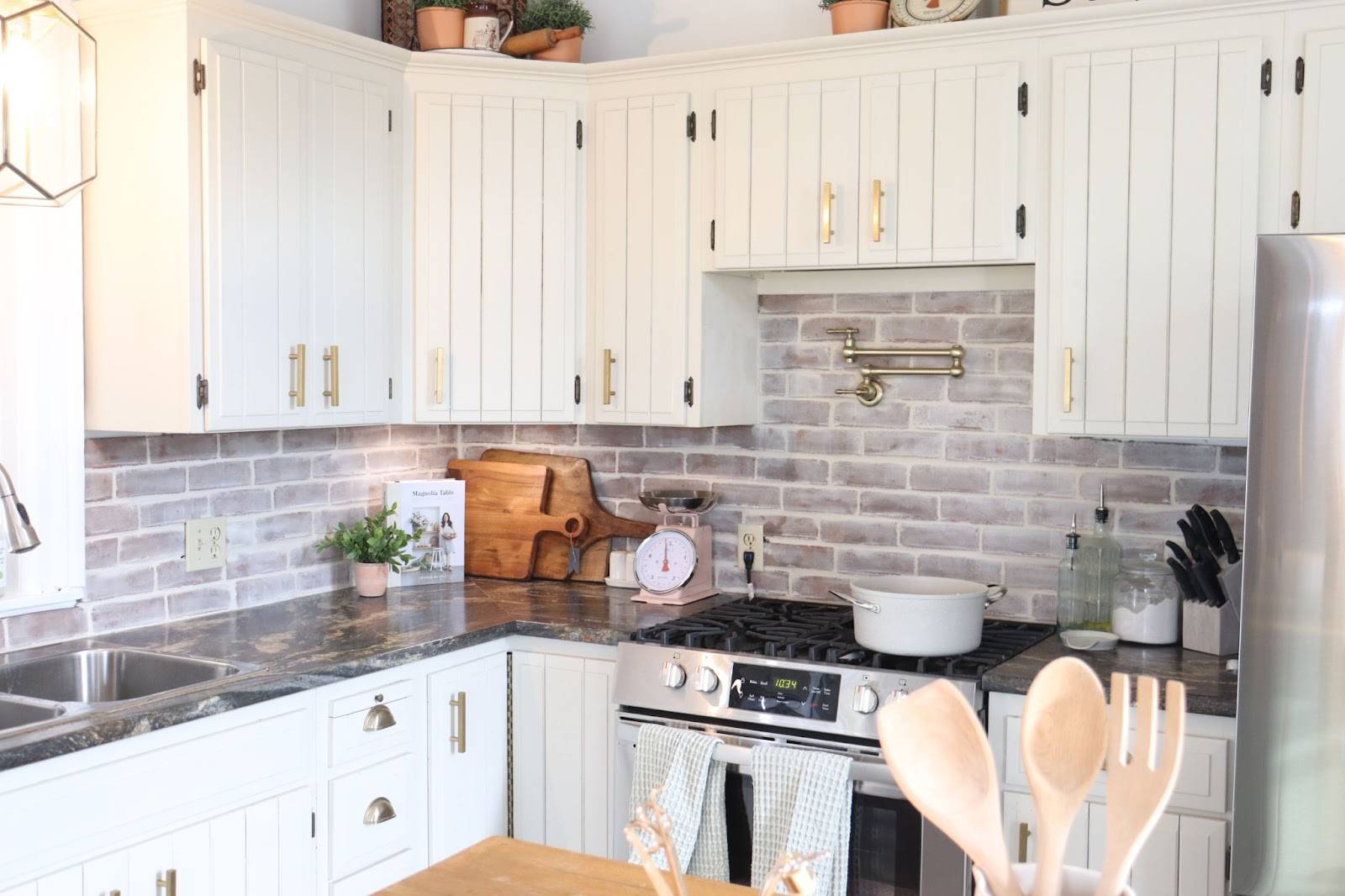 cream kitchen cabinets with dark countertops decorated brick backsplash with pot filler