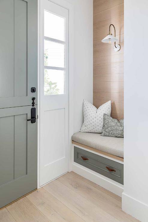 Small cottage entryway features a gray plank Dutch front door with side lights and a built in bench with drawers accented with brown leather pulls.