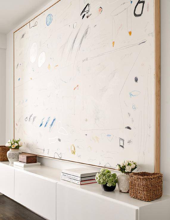 A large scale abstract art piece hangs over a long white buffet cabinet.