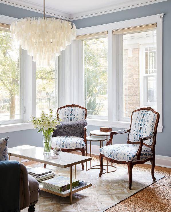 Make a room light and inviting by using soft blue walls with creamy white trim and neutral accents. The blue living room colors work well together and create an airy feel for a lit by a large white capiz chandelier over a brass and marble coffee table. Using multiples of items, such as the two white and blue French accent chairs, a gold parquet pattern rug and symmetry will give the room a sense of classic balance.