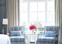 Master bedroom sitting area features gray French Louis Chairs with blue stripe cushions under a window with cream curtains.