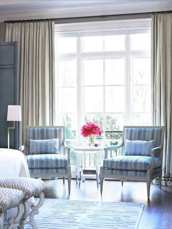 Master bedroom sitting area features gray French Louis Chairs with blue stripe cushions under a window with cream curtains.