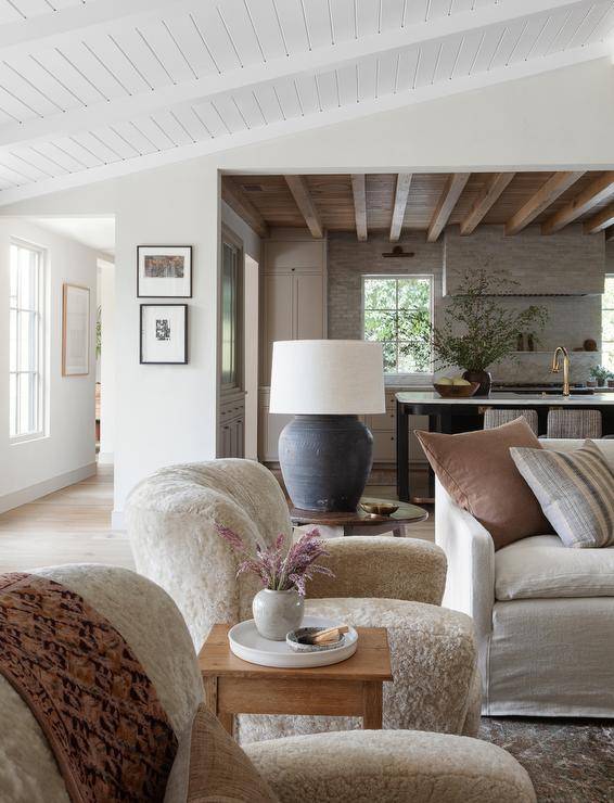 Ivory Teddy bear chairs sit beneath a vaulted plank ceiling on either side of a farmhouse accent table.