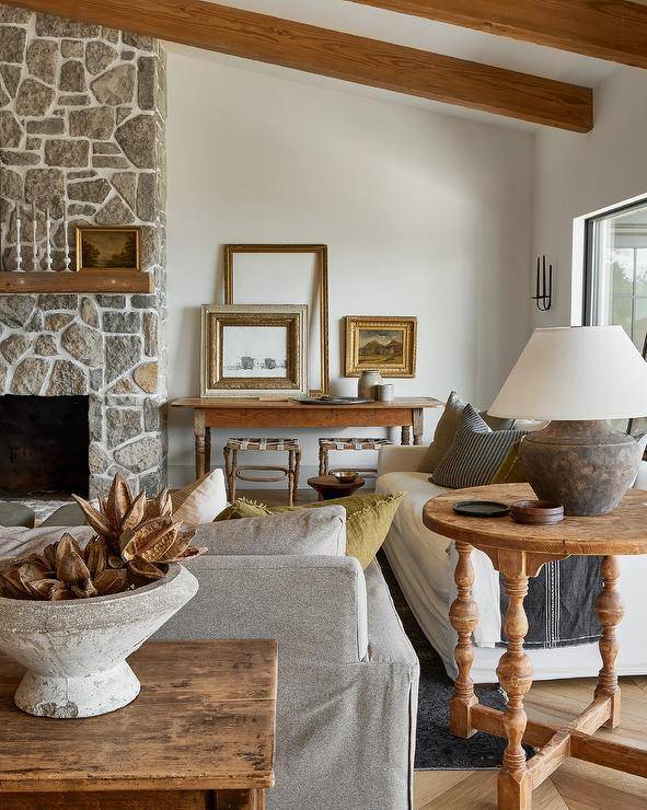 A rustic wooden mantel accents a gray stone fireplace fixed beside a farmhouse console table topped with layered art.