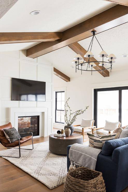 Board and batten fireplace displaying a mounted TV in a cottage living room finished with a vaulted ceiling and brown oak beams.