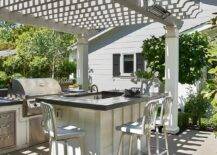 Gray pergola features an outdoor kitchen with1006 Navy counter stools at an island with a concrete countertop.