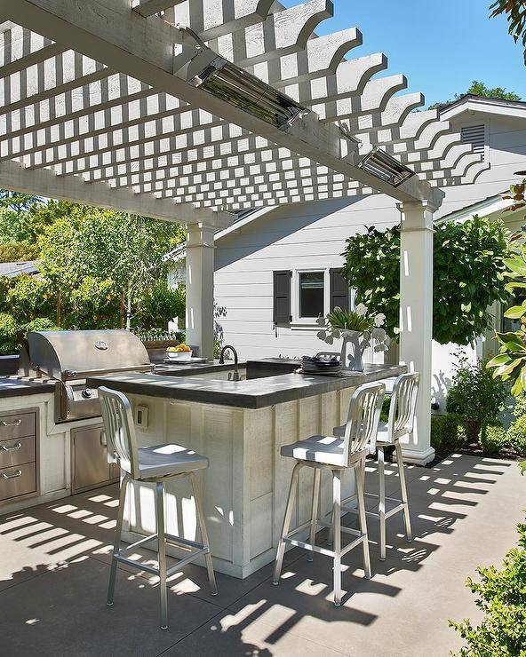 Gray pergola features an outdoor kitchen with1006 Navy counter stools at an island with a concrete countertop.