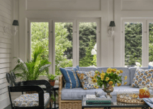 Sunroom features a rattan sofa with blue striped cushions accented with yellow floral pillows, a wrought iron coffee table and a glossy black accent chair atop black diamond pattern floor tiles under a lattice ceiling.