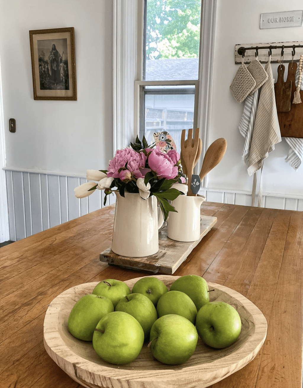 butcher block counter top with apples in wood bowl and flower arrangement