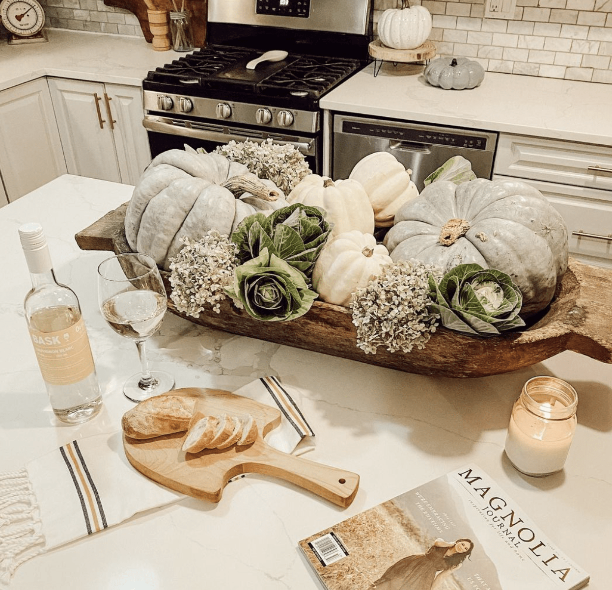 countertop decorated for fall with large pumpkins in a wood dough bowl