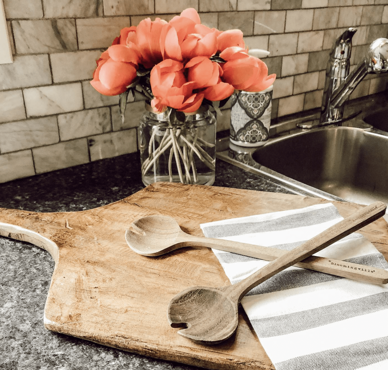 wood cutting board on countertop with flower arrangement and serving spoon