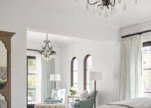 Master bedroom features a master sitting area with French crystal chandelier over gray accent chairs with a round cream tufted ottoman as coffee table atop a vintage rug.