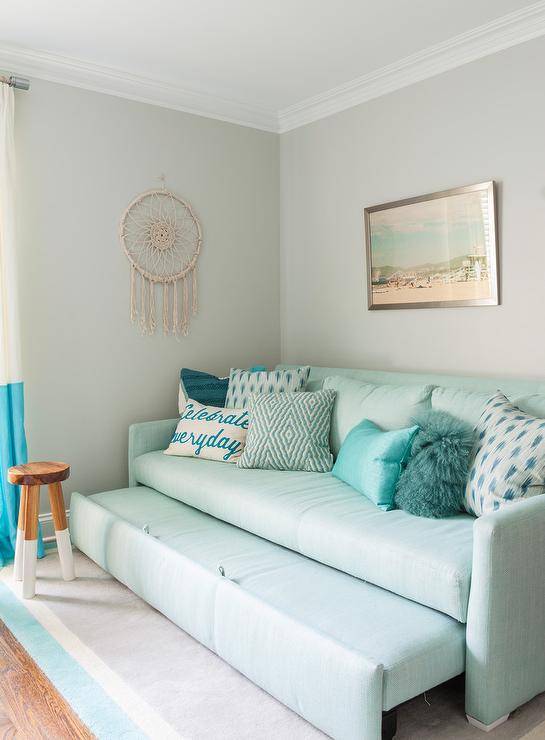 Serena & Lily Dip Dyed Stool beside an aqua blue sofa trundle bed decorated with various blue accent pillows against a gray wall in a girl's bedroom.