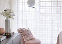 Modern bedroom features a pink velvet chair on a black and white geometric rug, a black dresser and white curtains, lit by a black and white floor lamp.