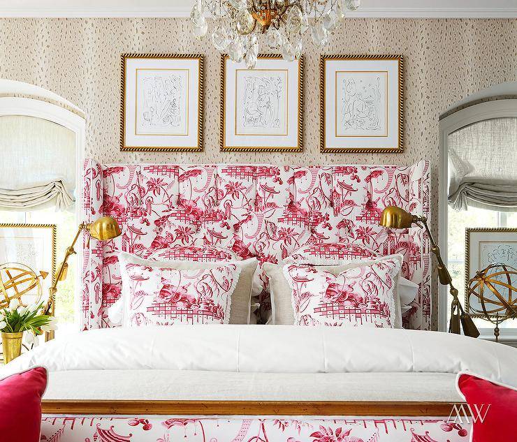 Pink pagoda toile pillows are placed on gray French bedding accenting a bed fitted with a pink toile wingback headboard. The headboard sits against a wall clad in animal print wallpaper beneath three gold framed art pieces.