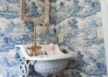 Incredible powder room with Sapphire Blue Toile wallpaper framing a distressed picture frame below a brass and frosted glass wall sconces. The ornate wall mounted sink with base and corbels painted in Benjamin Moore's Silver Lake pairs with a gooseneck brass faucet.