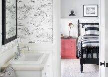 Cottage style kids bathroom with black and white toile wallpaper showcasing a bench between white washstands and a sink with vintage hook and spout faucets. Black inset framed medicine cabinets are mounted on the toile wallpaper finished with a two-light black sconce.