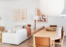 Dining room features a vintage oak dining table with vintage wood and leather chairs illuminated by an extra large rice paper lantern. A white sofa sits next to the dining room.