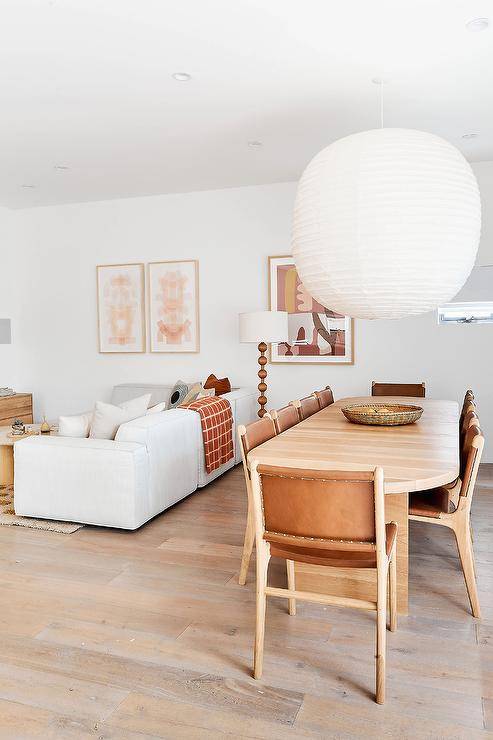 Dining room features a vintage oak dining table with vintage wood and leather chairs illuminated by an extra large rice paper lantern. A white sofa sits next to the dining room.