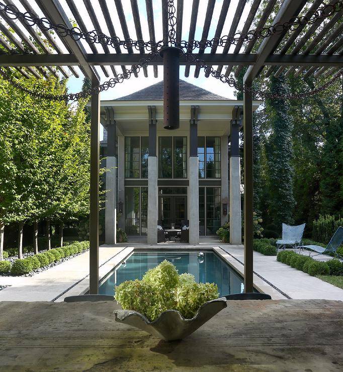 A black metal pergola is featured next to a rectangular in ground pool.