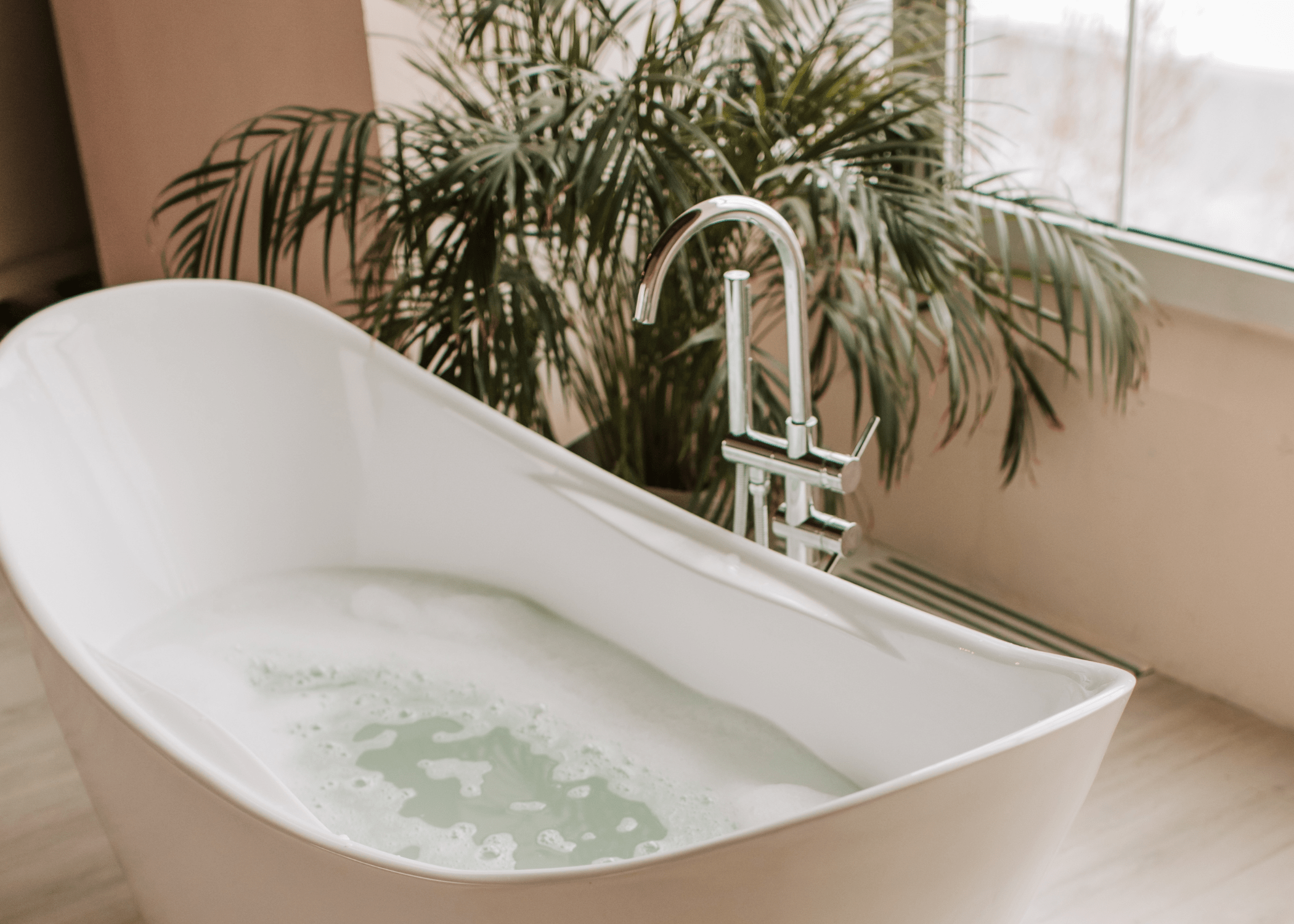 freestanding bathtub with floor faucet and greenery