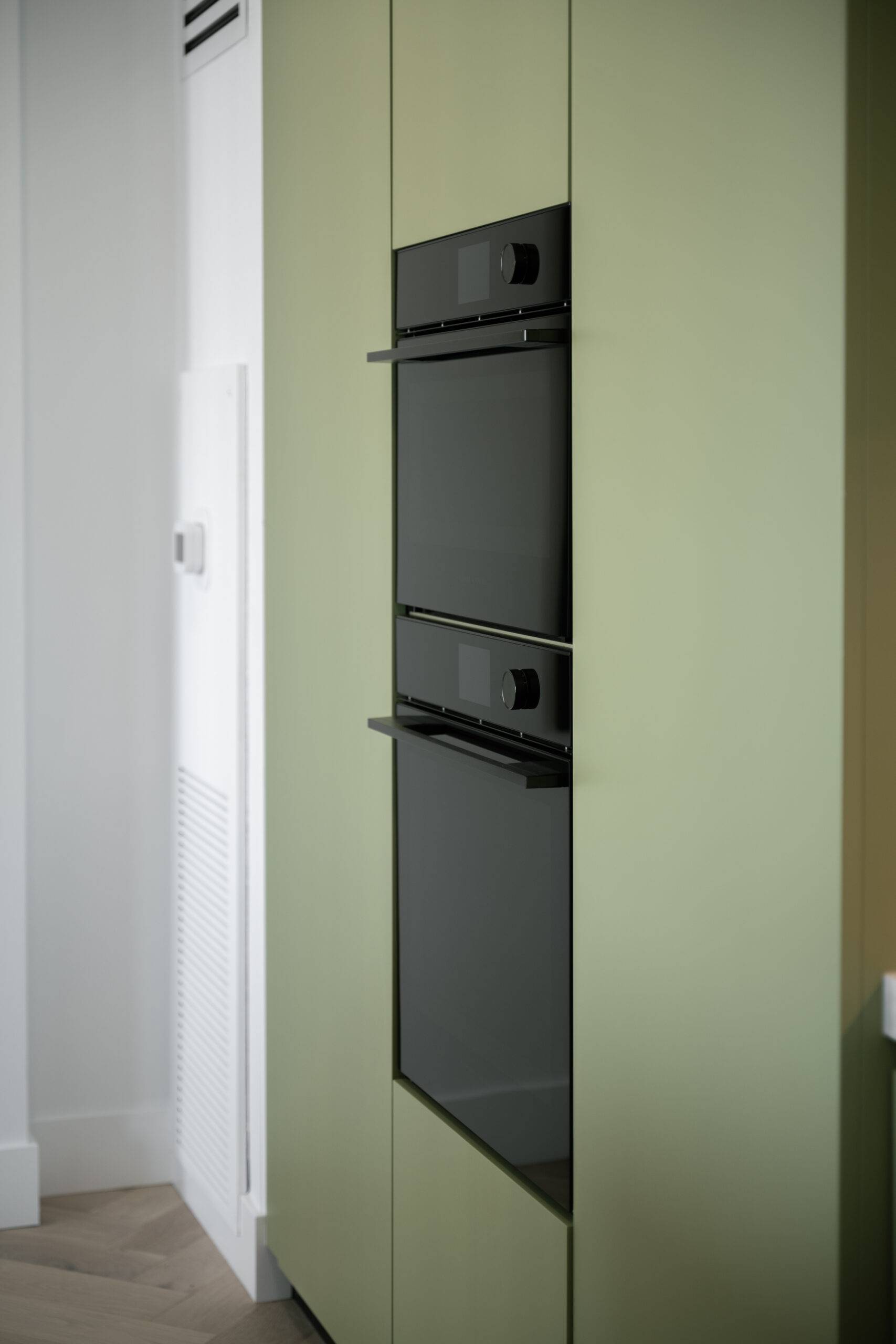 Sleek black appliances in a sage green kitchen.