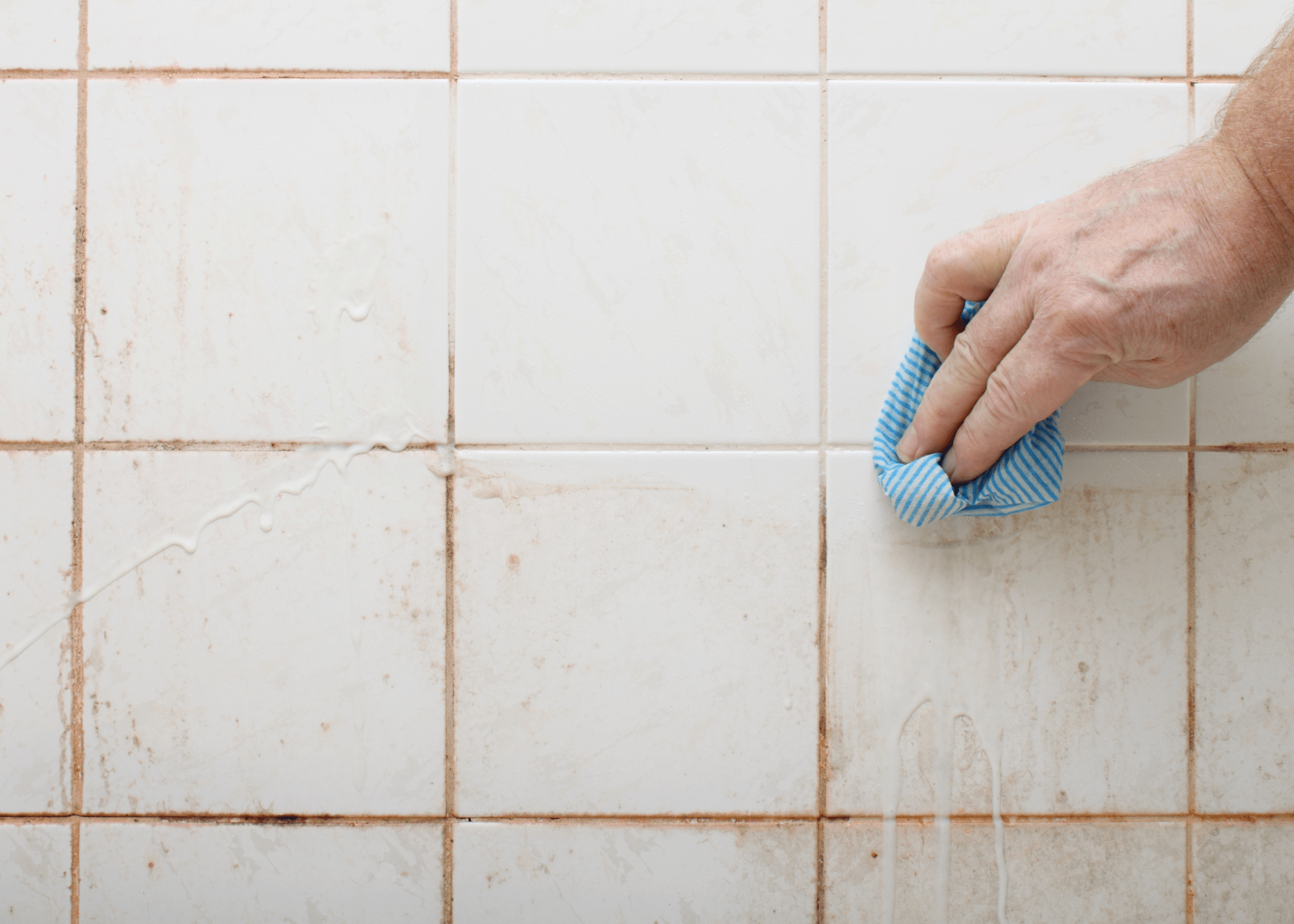 man cleaning soap scum off of shower wall