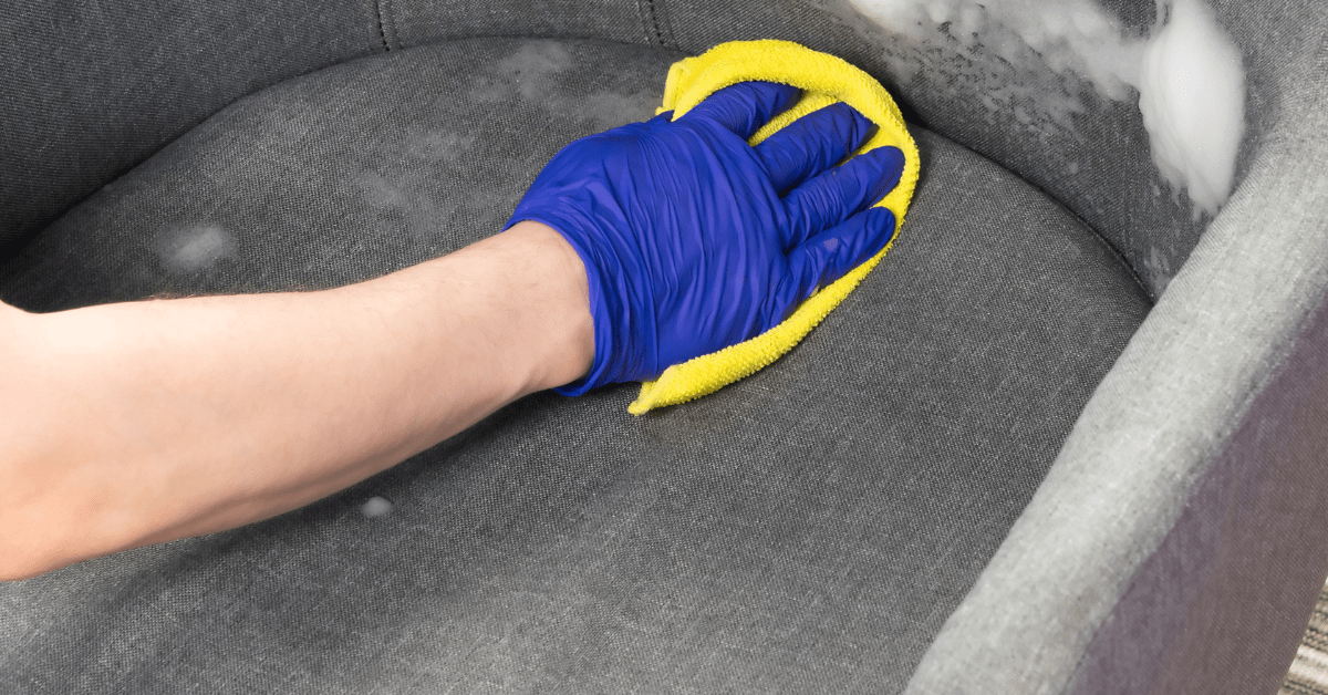 Hand wearing blue glove cleaning upholstery.