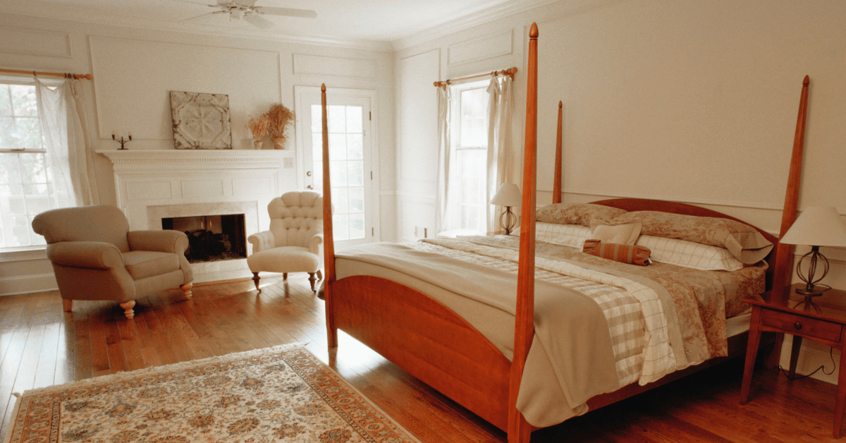 A wooden four poster bed in a large bedroom.