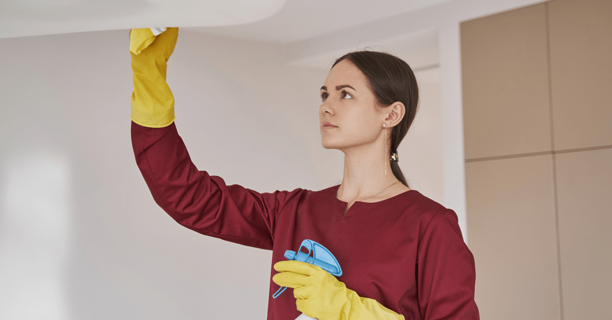 Woman cleaning ceiling fixture.