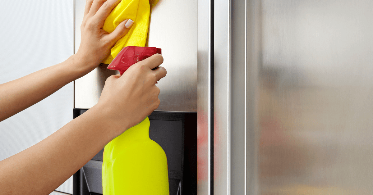 Using a cloth and spray to clean stainless steel fridge.