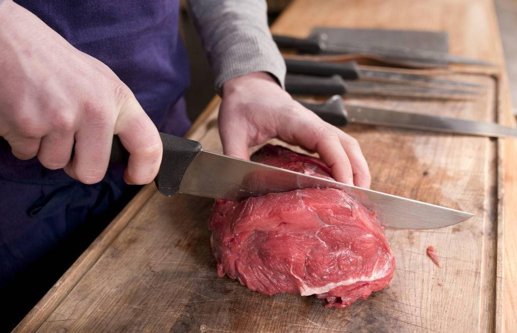 Close up shot of the hands of a butcher cutting a piece of meat.