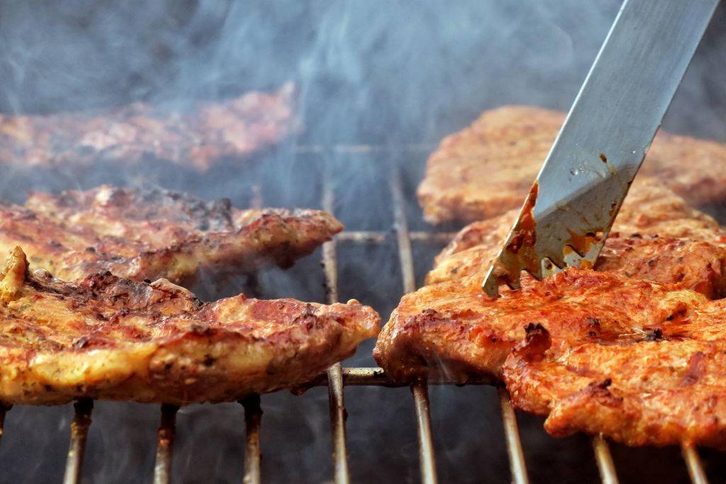 Steaks lie on a charcoal grill in a garden