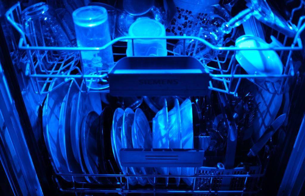 Washed dishes are in an open dishwasher with blue lighting