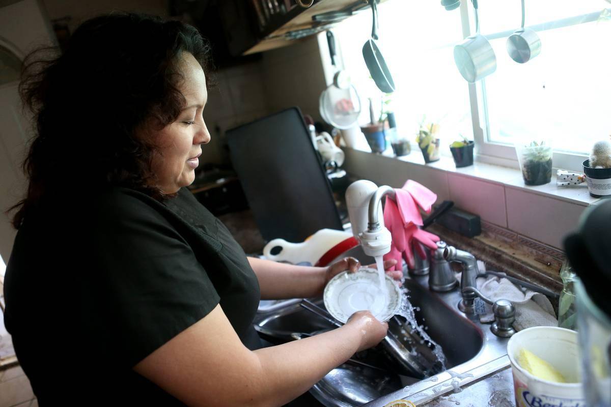 A woman washes dishes by hand in her kitchen.