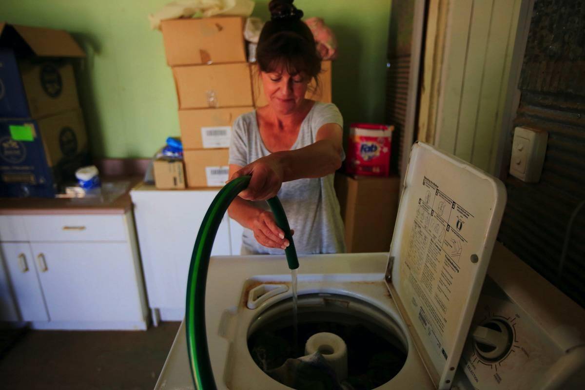 A woman fills her washing machine manually with a hose.