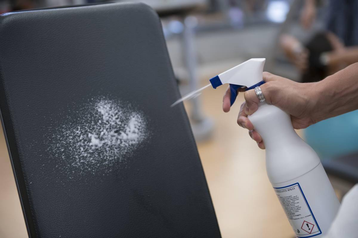 A man sprays a gym tool with a disinfectant.