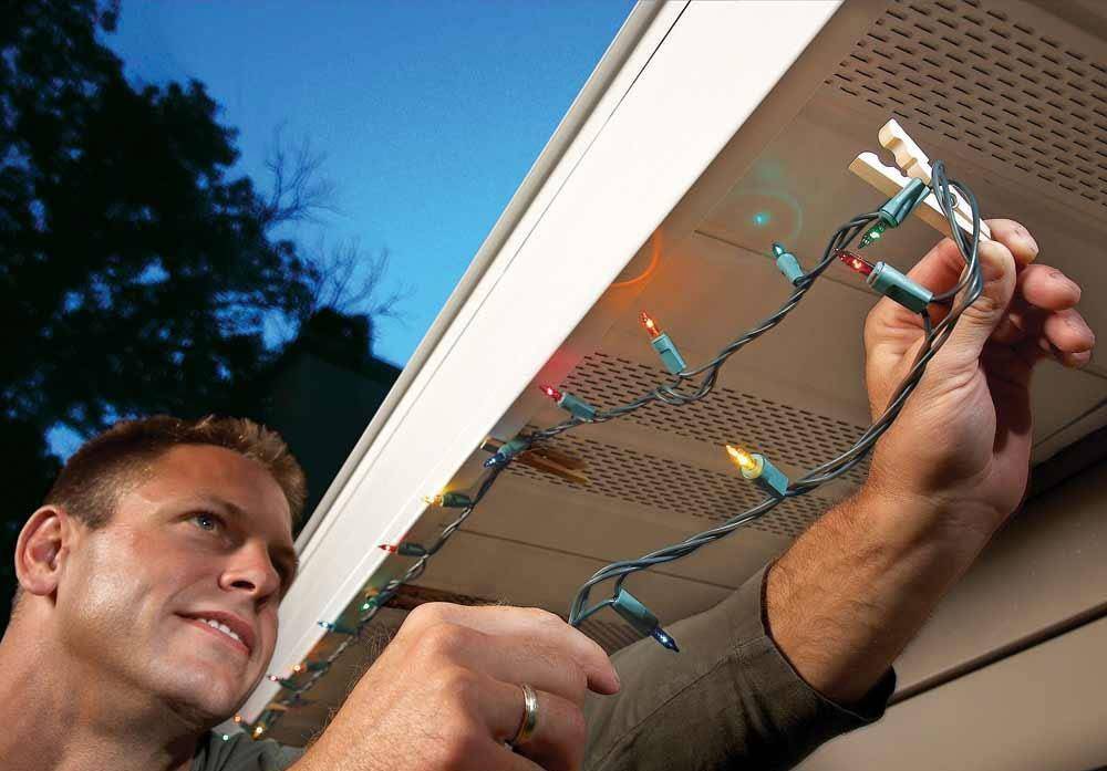 Man installing Christmas lights on underneath the house's gutter system.