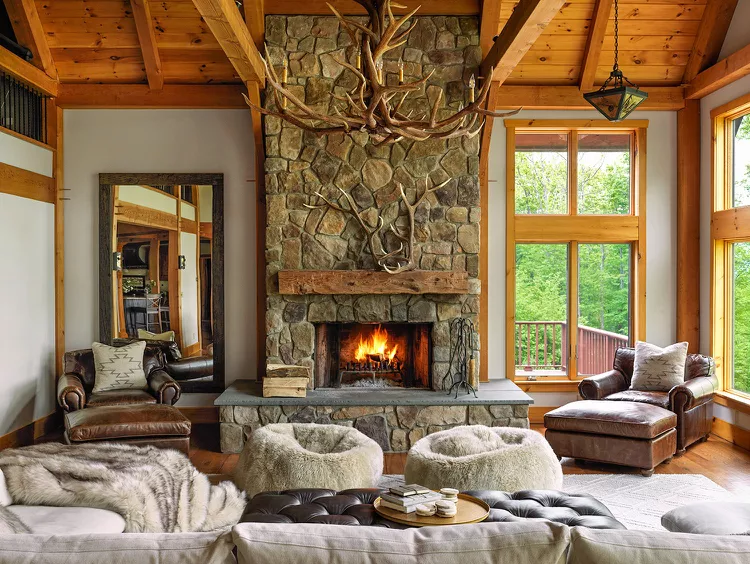 rustic living room featuring stone fireplace, fuzzy chairs and mounted antlers